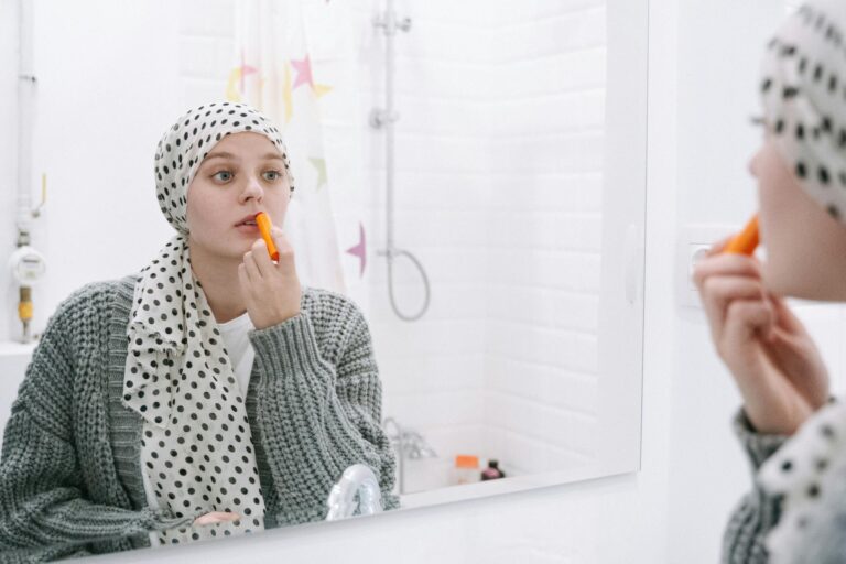 A woman in a headscarf applies lip balm, symbolizing strength and cancer awareness.