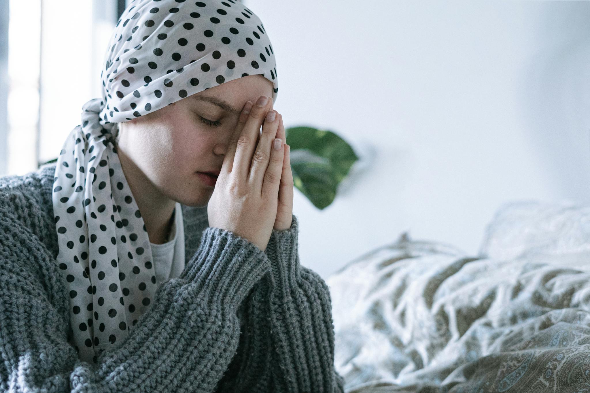 A woman wearing a scarf prays indoors, symbolizing hope and recovery from cancer.