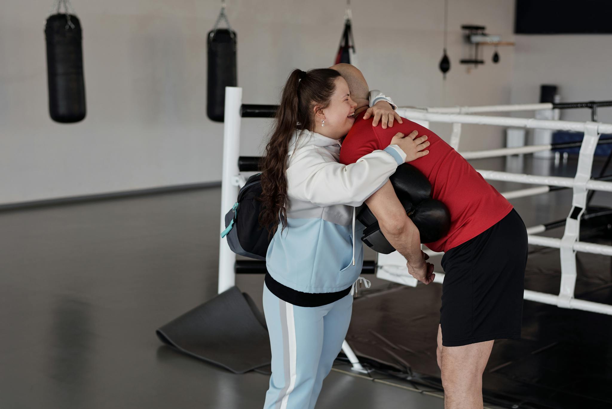 A woman with Down syndrome hugging her boxing trainer in the gym.