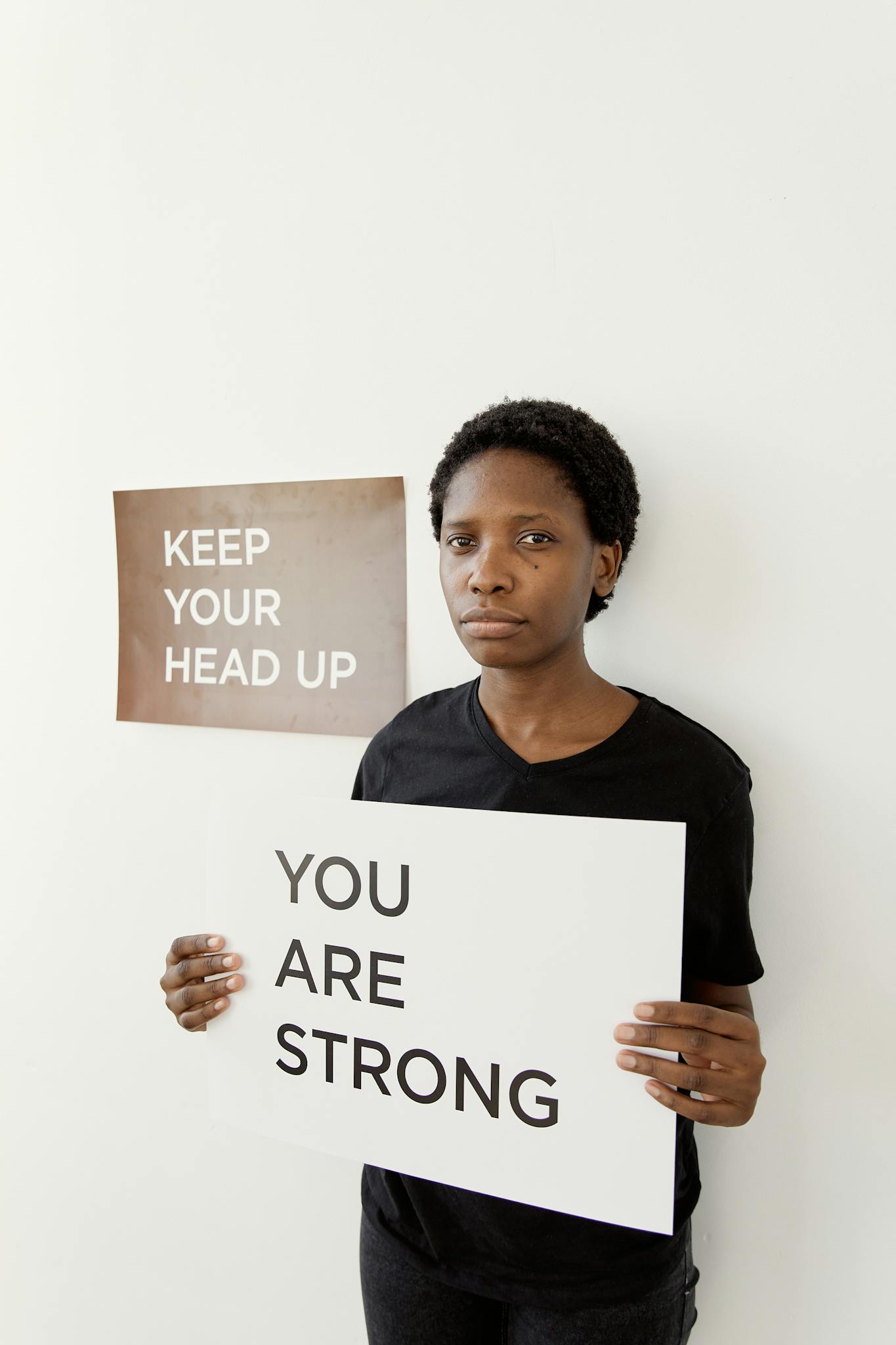 Black woman holding signs with motivational messages indoors, promoting mental strength.